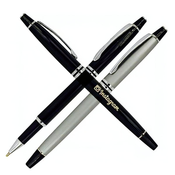 Two Xpress Rollerball Metal Pens by PensXpress, one black and one silver, are crossed in an X shape. The silver pen displays the Instagram logo and name in gold. Both feature metallic clips and accents—ideal for promotional events.